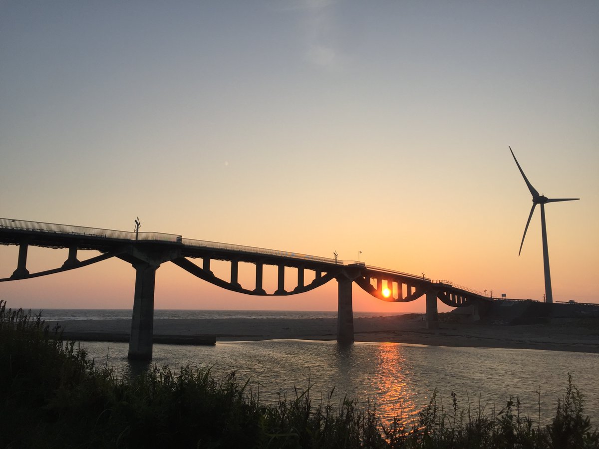 VIVANTのアーチが連なる橋と、右手に立つ風車、橋の向こうの夕日