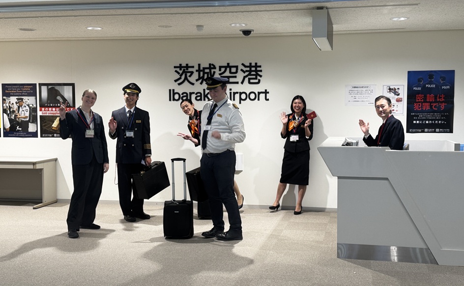 VIVANTの鳥取ロケ地の「茨城空港」「Ibaraki Airport」と書かれた表示の前に立つ、制服やスーツ姿の人たち