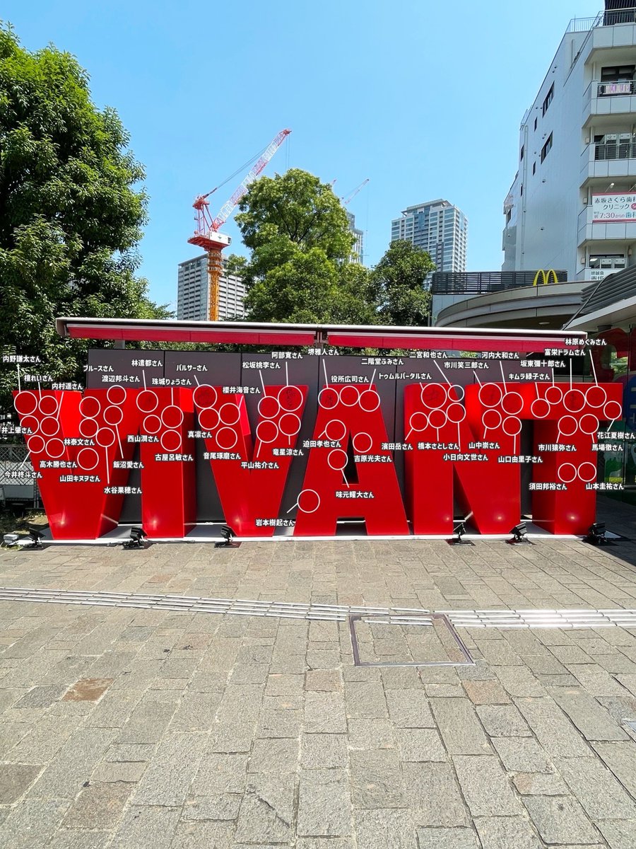 VIVANTのモニュメントの石畳の上に置かれた赤いVIVANTの文字のモニュメント。表面の白い丸の印ごとに、さんを付けた名前が添えられている
