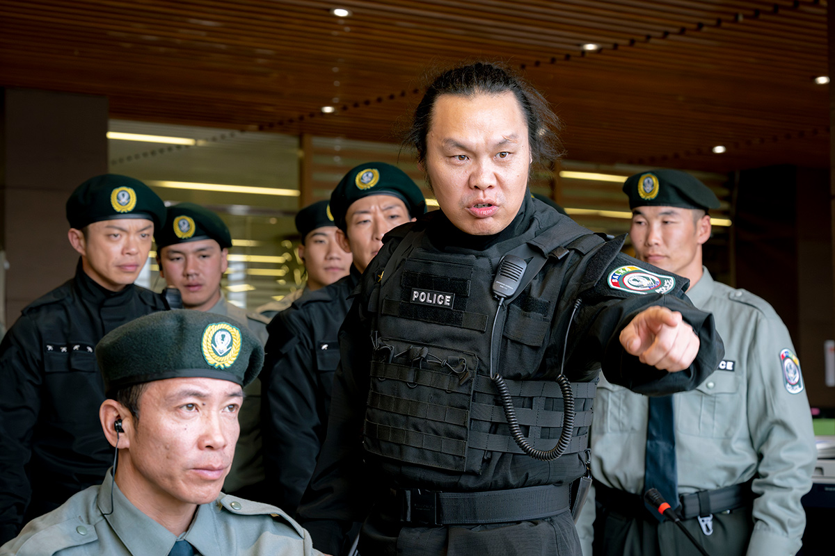 チンギスの「POLICE」のベストの男性が、大勢の警察官の前で前方を指さす場面(第7話の場面写真)