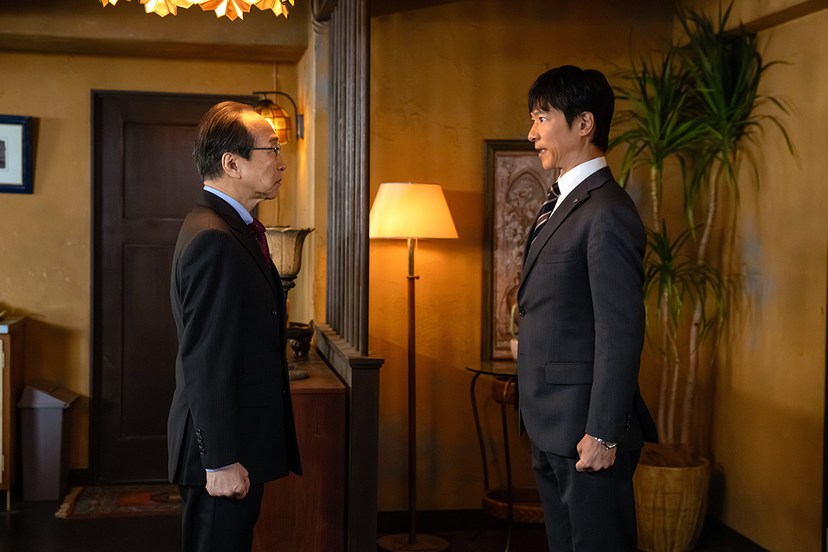 VIVANT第12話の明かりのともる部屋で、スーツ姿の男性2人が向かい合って立っている場面