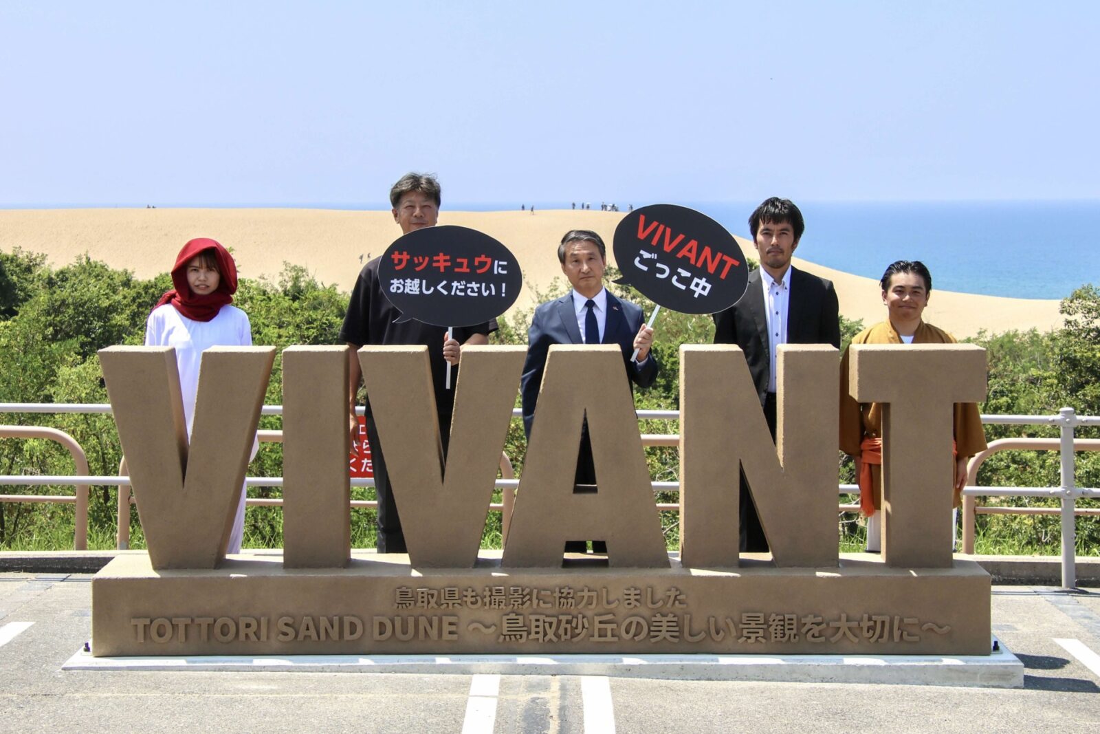 VIVANTのイベントの台の上に並ぶ薄い茶色の立体のVIVANTの文字。台の正面に鳥取県も撮影に協力しましたと刻まれ、奥に砂丘と青い海が見える