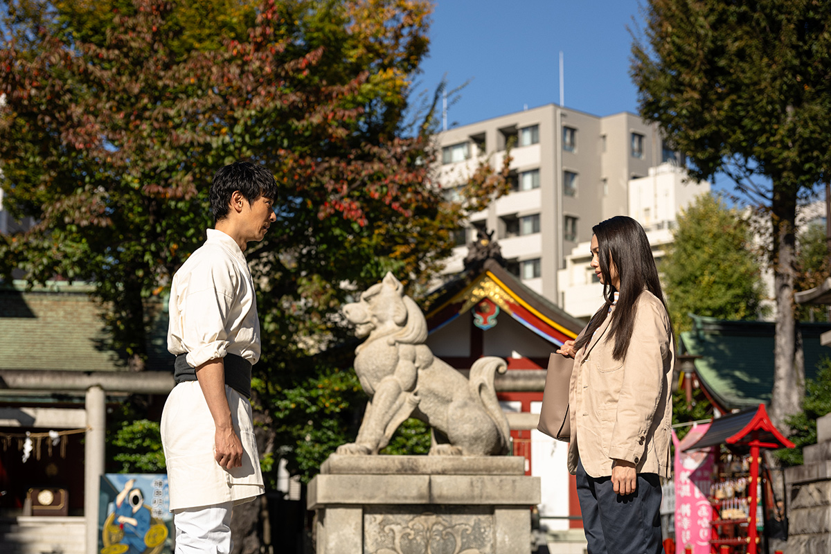 薫の第11話の場面写真。神社の境内で、狛犬の像をはさんで白い服の男性と長い黒髪の女性が向き合う