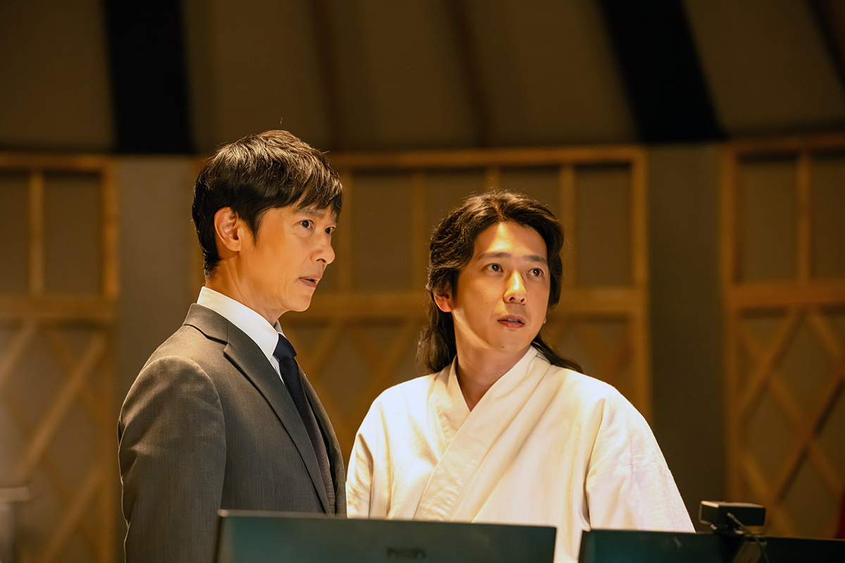 黒須のスーツの男性と白い服の長い髪の男性が並んで立つ場面(第12話の場面写真)