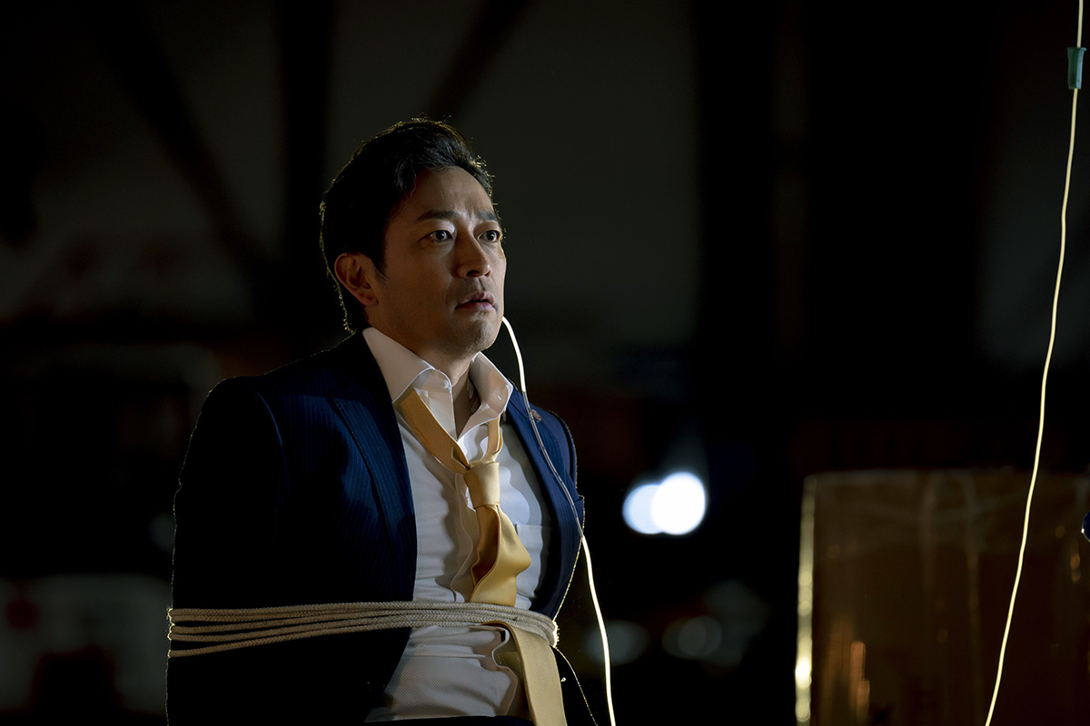 黒須の紺のスーツの男性が胴に縄を巻かれている場面(第12話の場面写真)