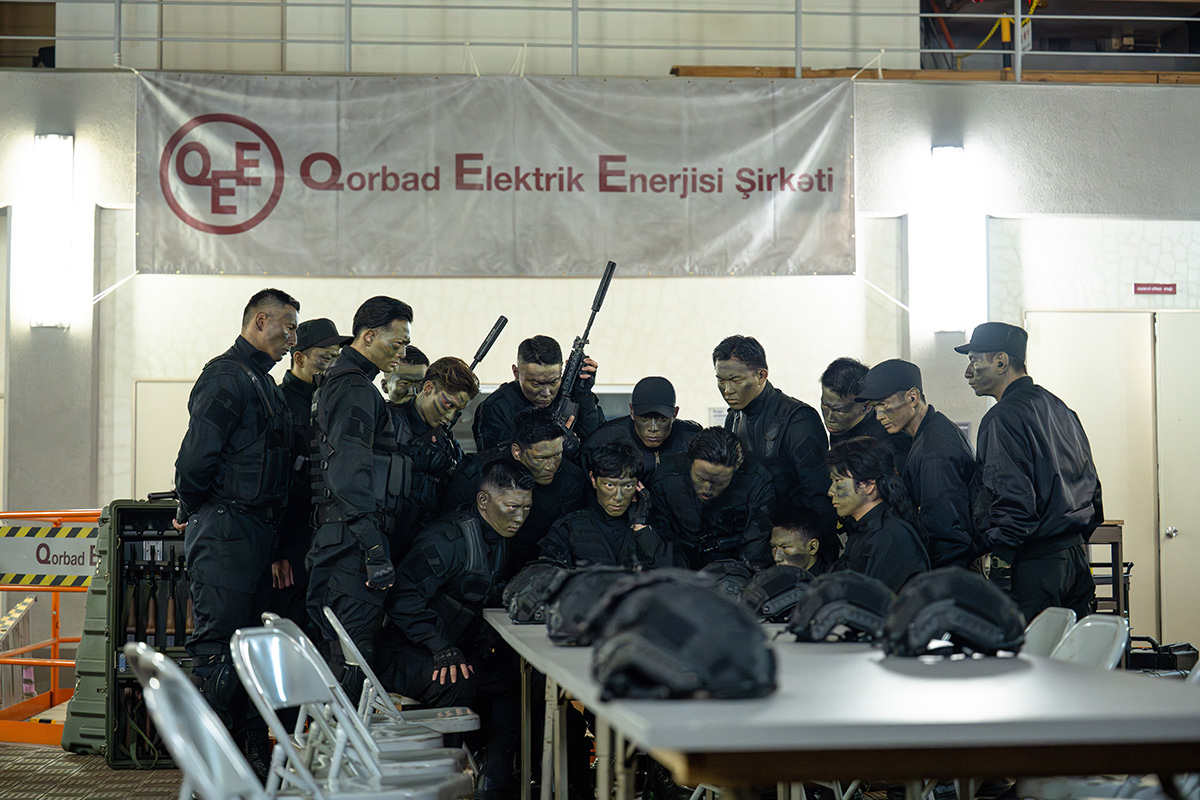 VIVANTの「Qorbad Elektrik Enerjisi Şirkəti」と書かれた横断幕の下で、机のまわりに集まる黒い服の十数人