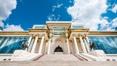 VIVANTのモンゴルの青空の下、柱の並ぶ白い大きな建物と、正面の階段の上に座った人物の像