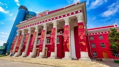 VIVANTのモンゴルの白い柱が並ぶ正面に赤い垂れ幕が下がった、赤い壁の建物