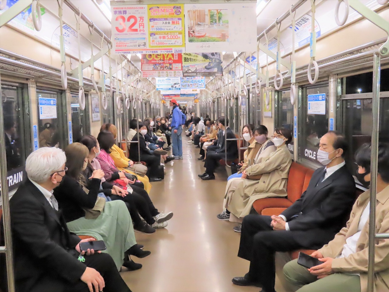 VIVANTの豊橋ロケ地の電車の車内の両側の座席に、大勢の人が並んで座っている様子
