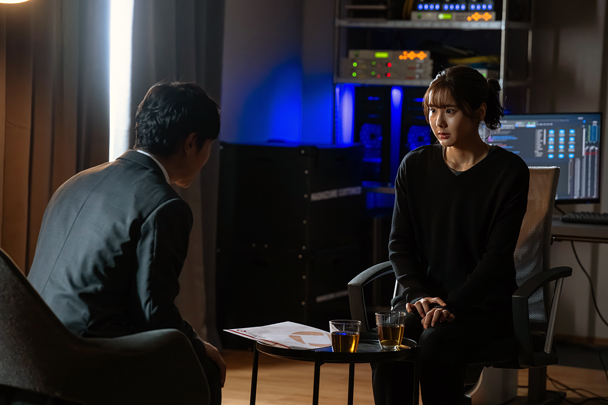 長野専務の第13話の場面写真。黒いセーターの女性が椅子に座り、スーツ姿の人と向き合っている