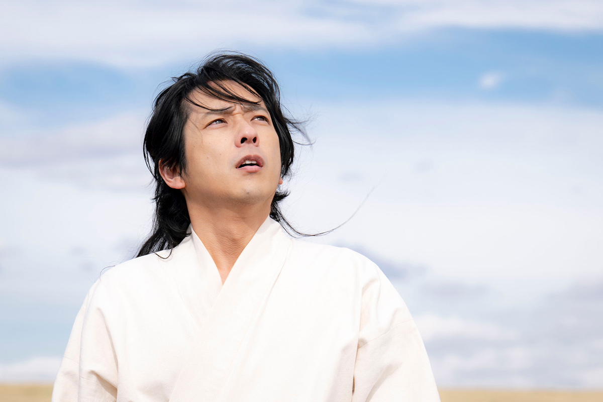 ノコルの最終回の場面写真。白い服の長い髪の男性が、青空の下で空を見上げている