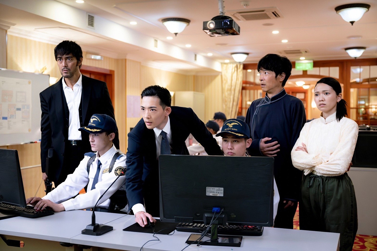 野崎のパソコンの画面を囲んでのぞき込むスーツの男性たちと制帽の人物(第2話の場面写真)