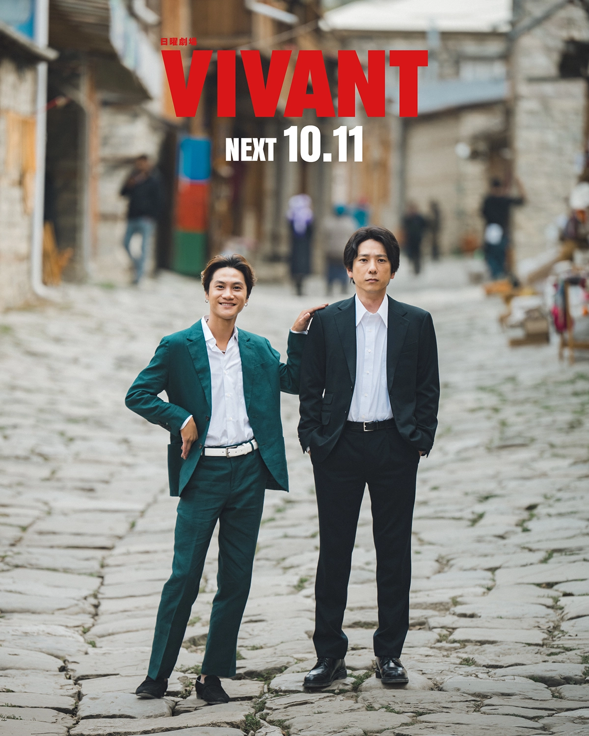 VIVANTの石畳の通りに緑色のスーツと黒いスーツの2人が立ち、赤い文字でVIVANT、白い文字で「NEXT 10.11」と入った画像