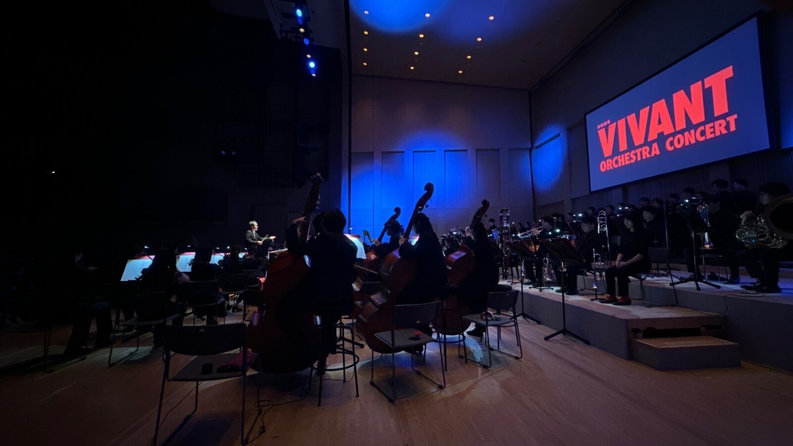 VIVANTの暗いホールのステージの奥のスクリーンに映るVIVANT ORCHESTRA CONCERTの文字と、手前に並ぶ奏者