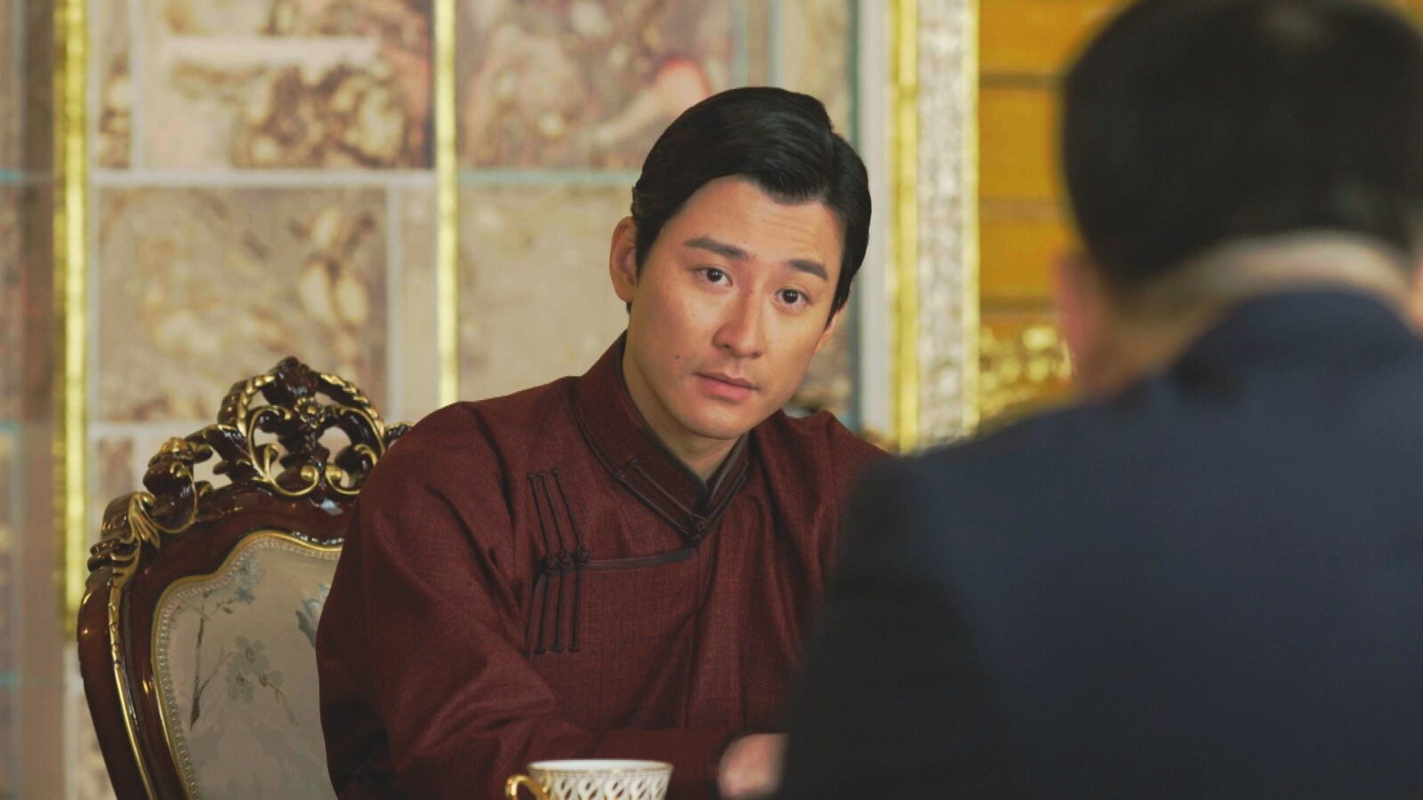 悪役大会議室の赤茶色の詰め襟の上着の男性が、金色の飾りのある椅子に座っている