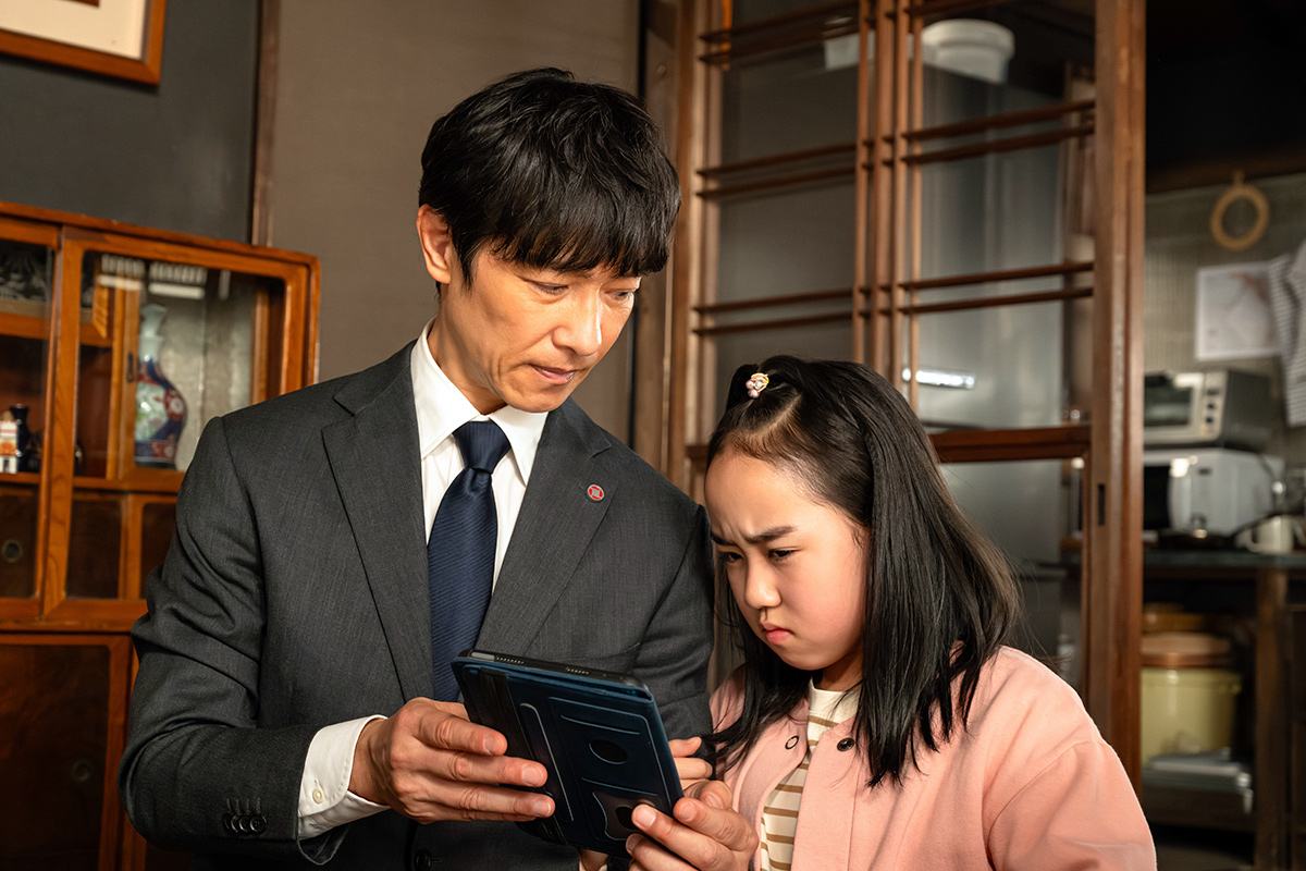 VIVANT第17話のスーツ姿の男性と少女が、タブレットを一緒にのぞき込む場面